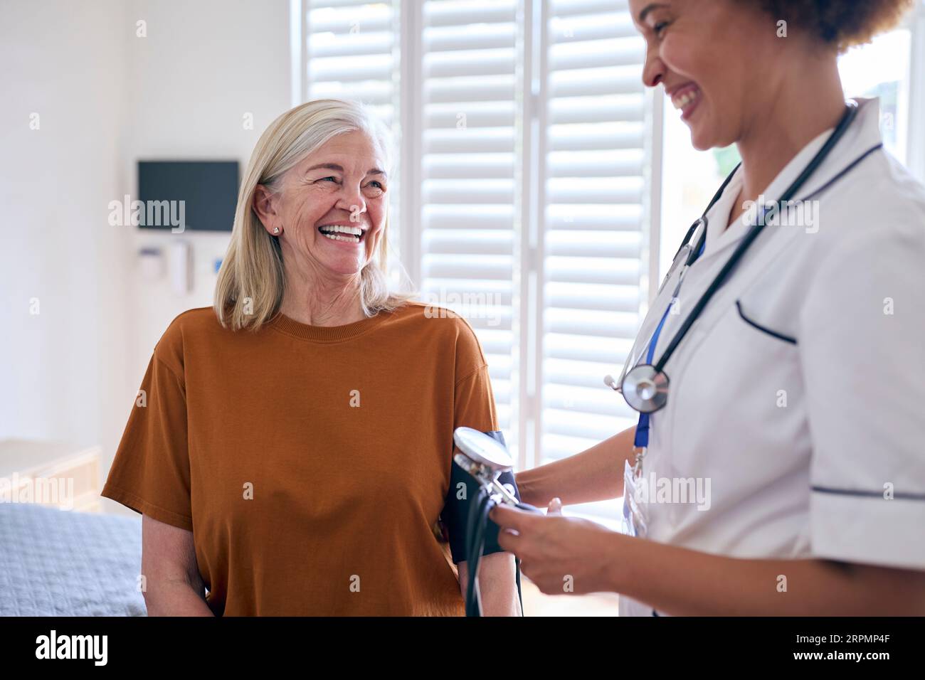 Infermiera femminile che indossa l'uniforme che prende la pressione sanguigna della donna anziana nella stanza privata dell'ospedale Foto Stock