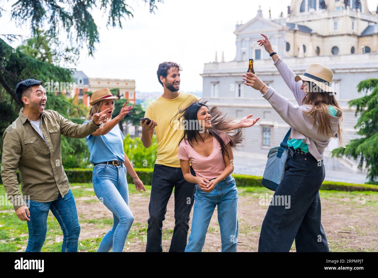 Gruppo multietnico di amici che festeggiano in un parco cittadino con birre. divertimento estivo, un amico arriva con il frigo e le birre fredde Foto Stock