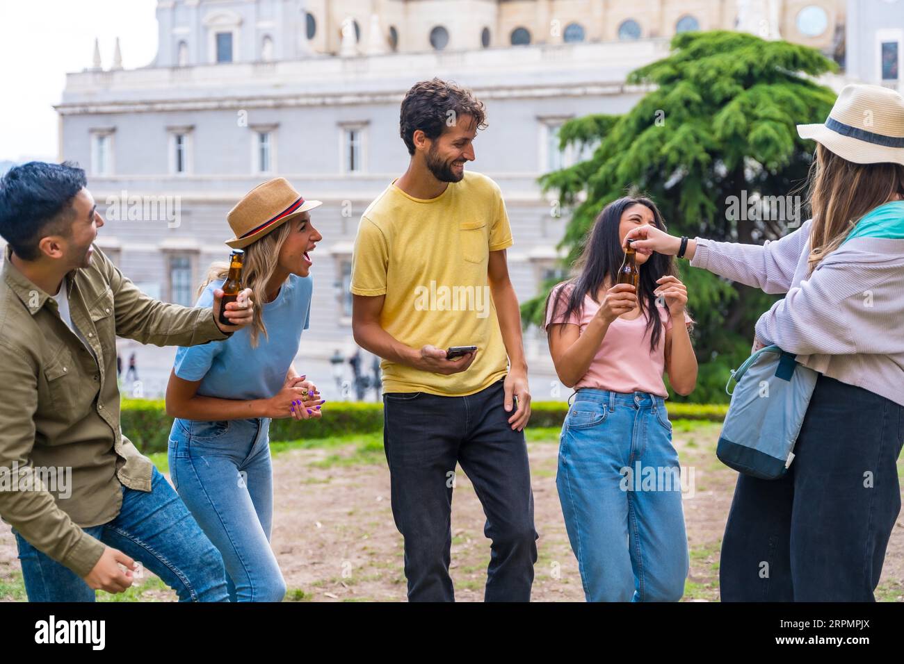 Gruppo multietnico di amici che festeggiano in un parco cittadino con birre. divertimento estivo, saluti al nuovo amico che è arrivato Foto Stock