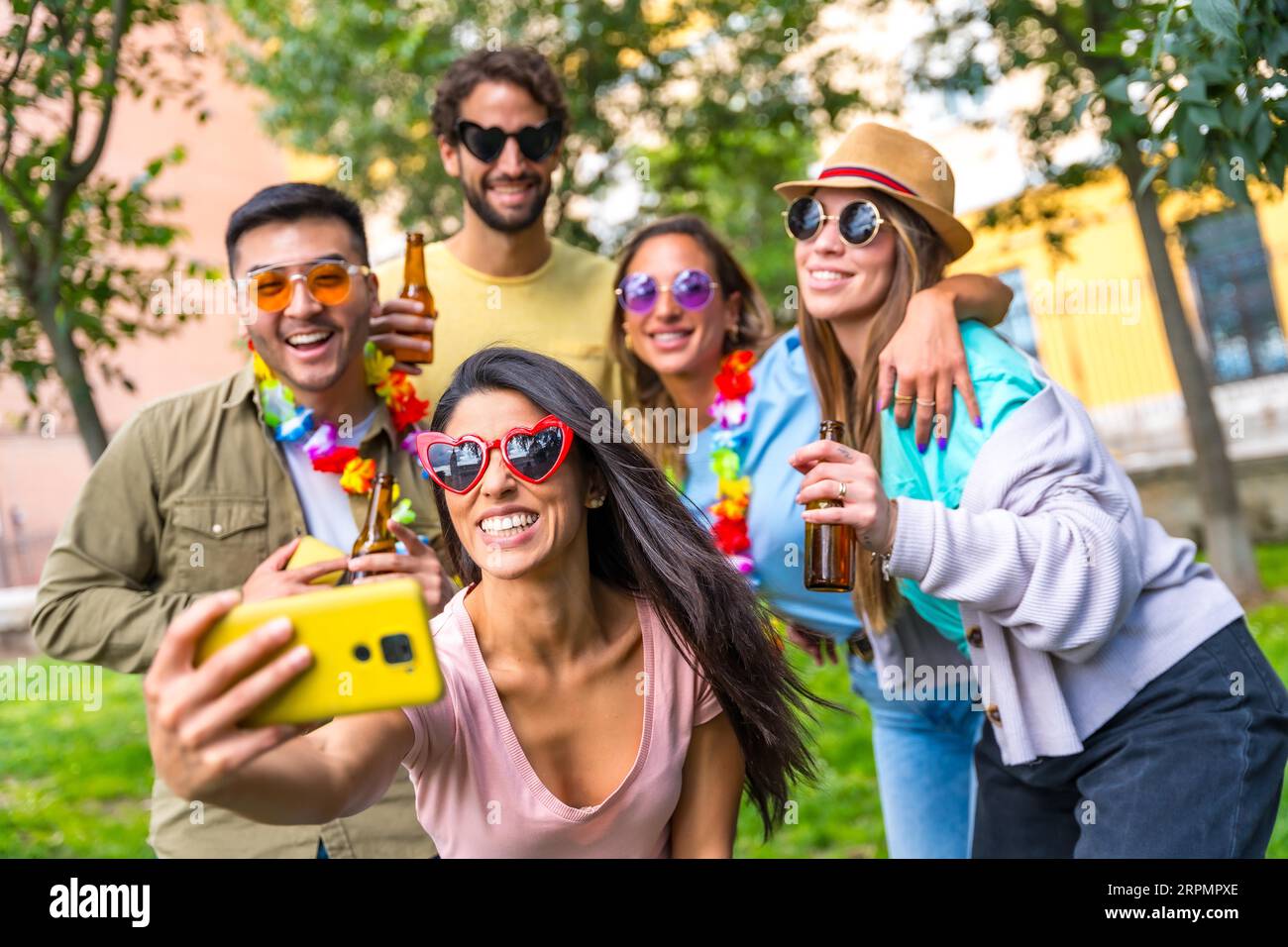 Gruppo multietnico di amici che festeggiano nel parco cittadino per scattare un selfie, un'amicizia e un concetto di divertimento indossando occhiali da sole durante una festa di compleanno Foto Stock