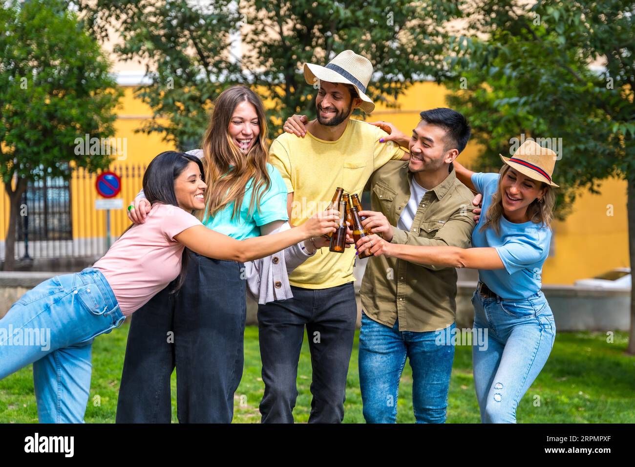 Gruppo multietnico di amici che festeggiano in un parco cittadino brindando bottiglie di birra Foto Stock