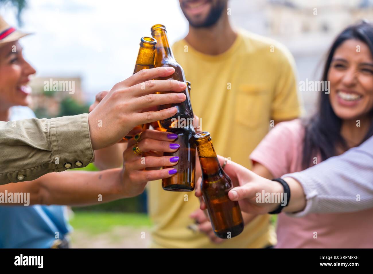 Gruppo multietnico di amici che festeggiano in un parco cittadino con birre. tostare con i biberon Foto Stock
