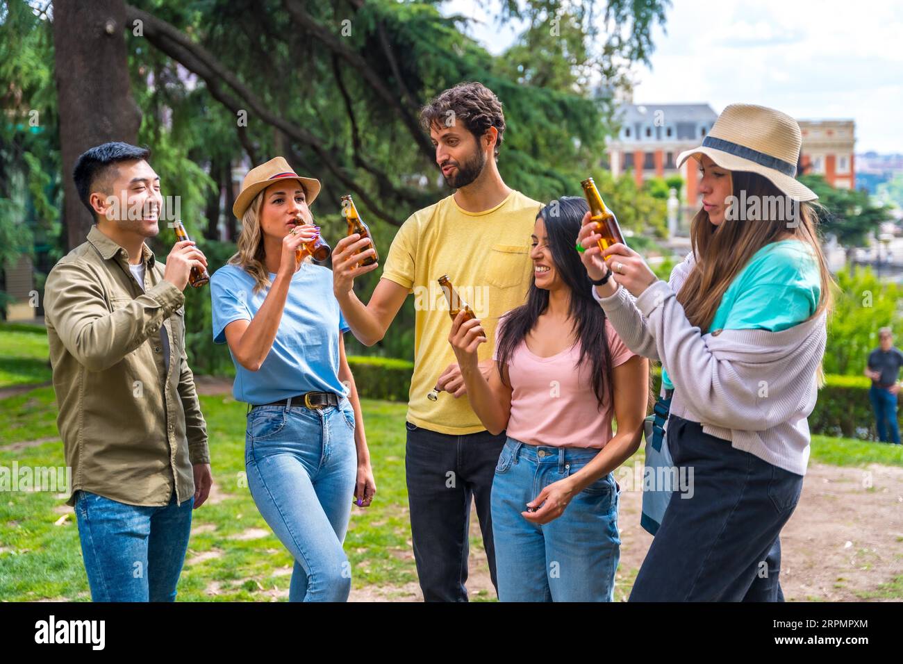 Gruppo multietnico di amici che festeggiano in un parco cittadino con birre. Amici che bevono birra fredda Foto Stock