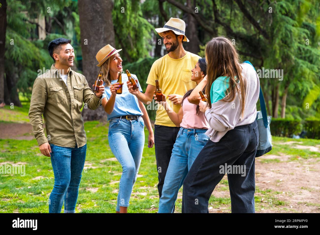 Gruppo multietnico di amici che festeggiano in un parco cittadino con bottiglie di birra Foto Stock
