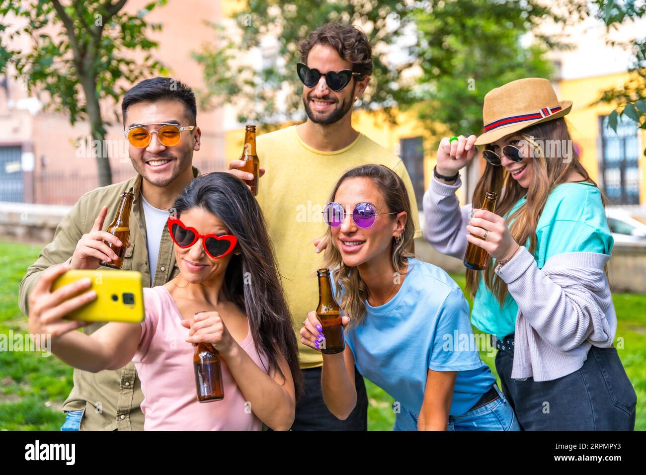 Gruppo multietnico di amici che festeggiano nel parco cittadino per scattare un selfie, un'amicizia e un concetto di divertimento indossando occhiali da sole e bevendo birra Foto Stock