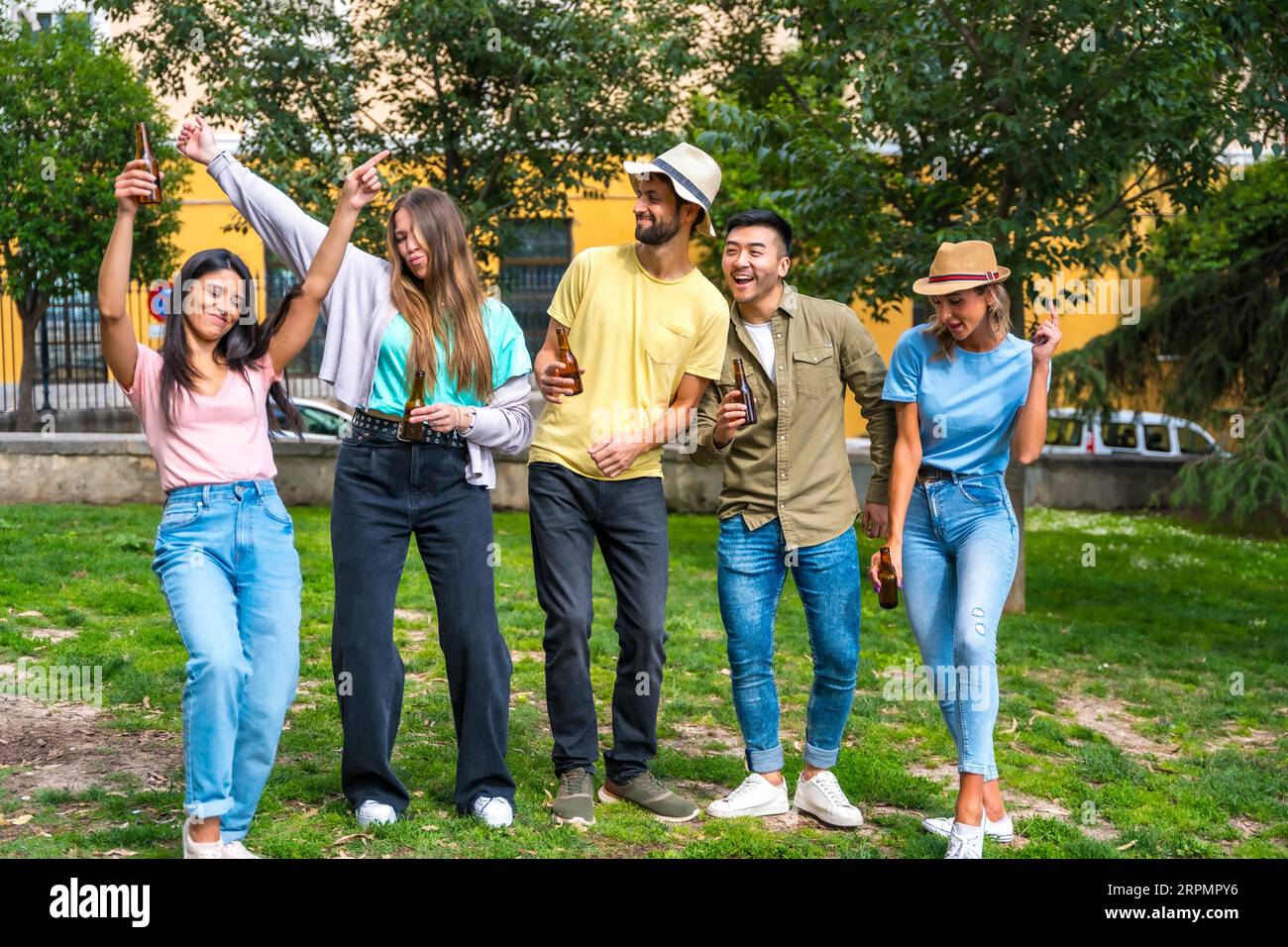 Gruppo multietnico di amici che festeggiano in un parco cittadino divertendosi con bottiglie di birra Foto Stock