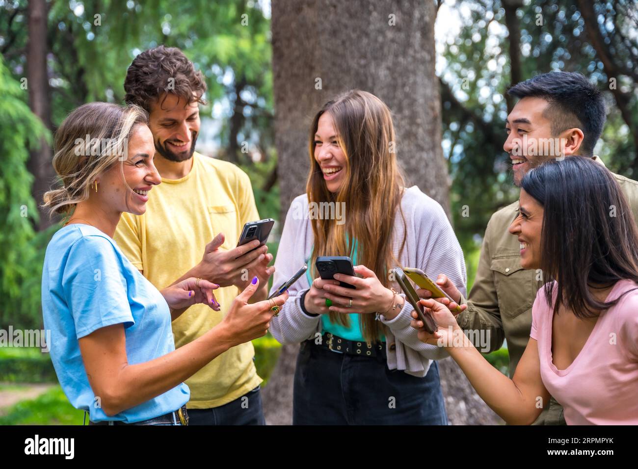 Gruppo multietnico sorridente con telefoni che guardano Internet o social network nel parco, concetto tecnologico Foto Stock