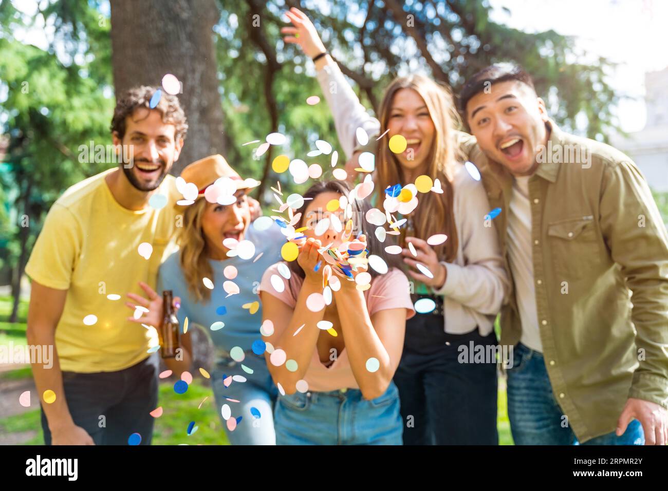 Ritratto di un gruppo multietnico di festeggiamenti che lanciano coriandoli sorridendo nel parco, concetto di divertimento con gli amici Foto Stock