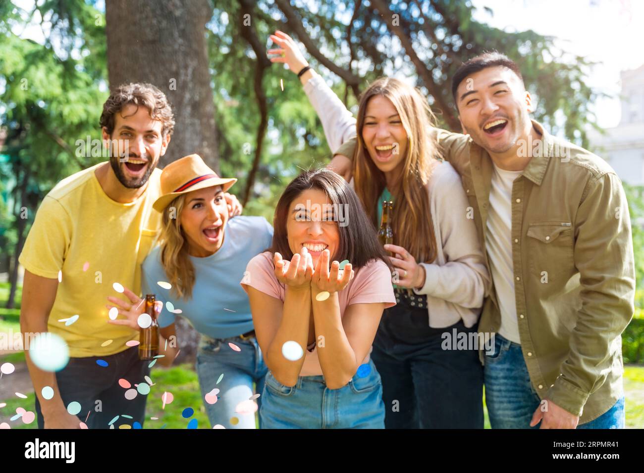 Gruppo multietnico di festeggiamenti che lanciano coriandoli sorridendo nel parco, concetto di divertimento con gli amici Foto Stock