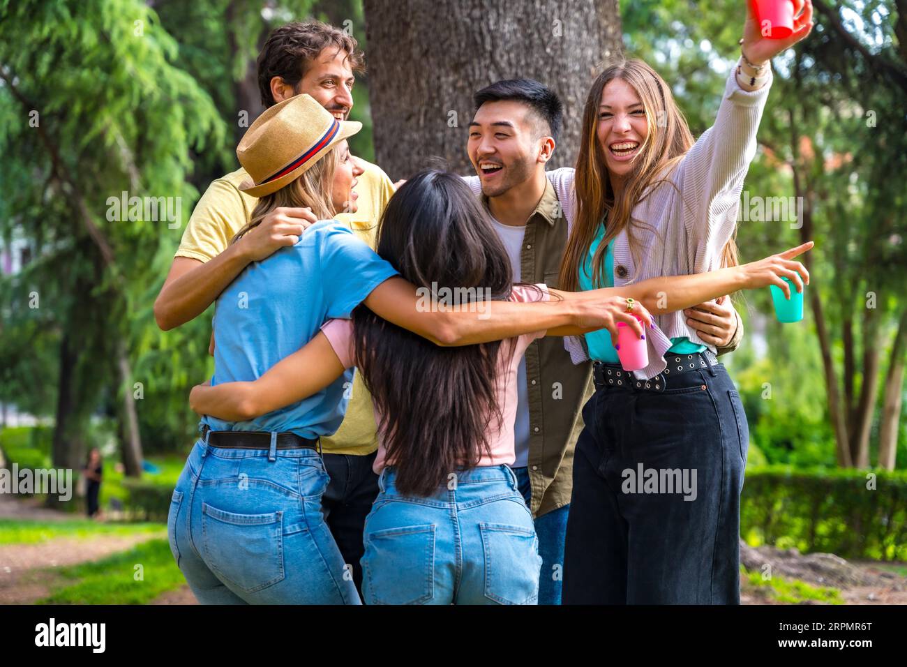 Gruppo multietnico di festa di compleanno nel parco cittadino abbracciando un simbolo di amicizia per sempre e sorridendo molto Foto Stock
