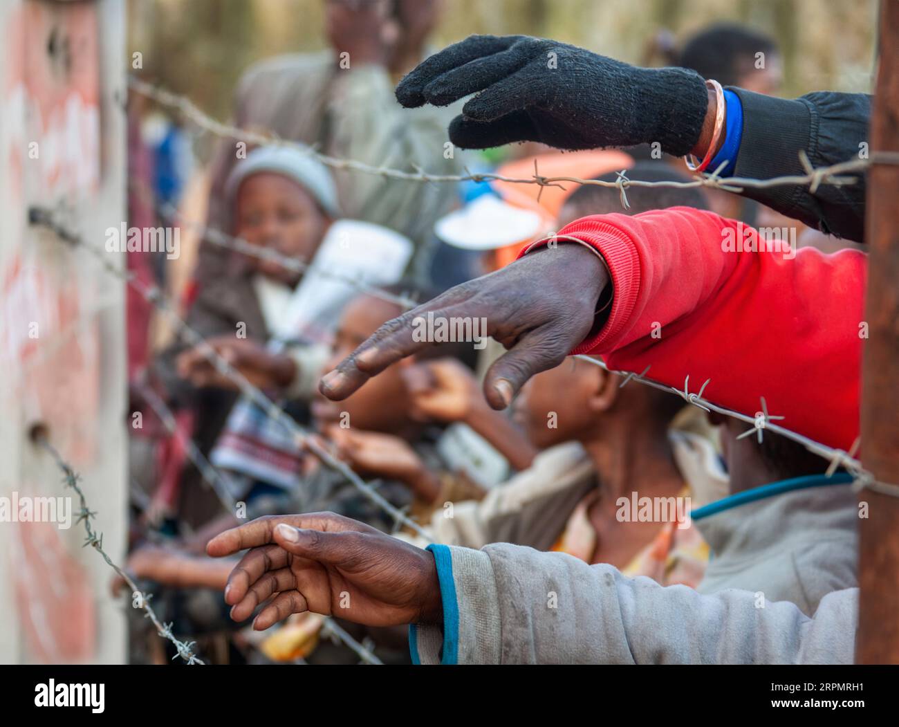 disordini sociali nel continente africano, folla di persone mani viste attraverso la recinzione di filo spinato Foto Stock