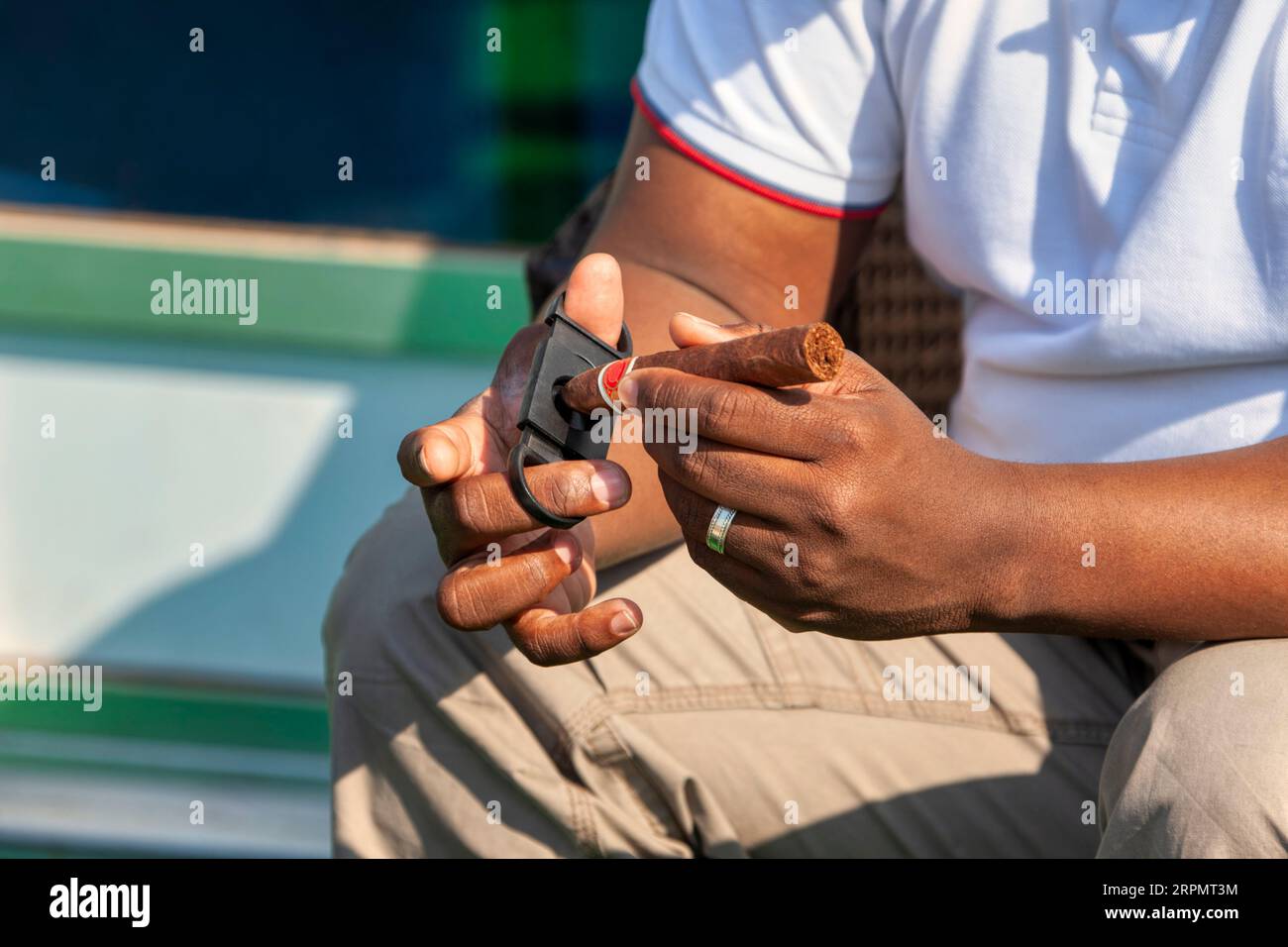 Un uomo d'affari afro-americano si trovava all'aperto usando un tagliaerba Guillotine per tagliare un sigaro di alta qualità Foto Stock