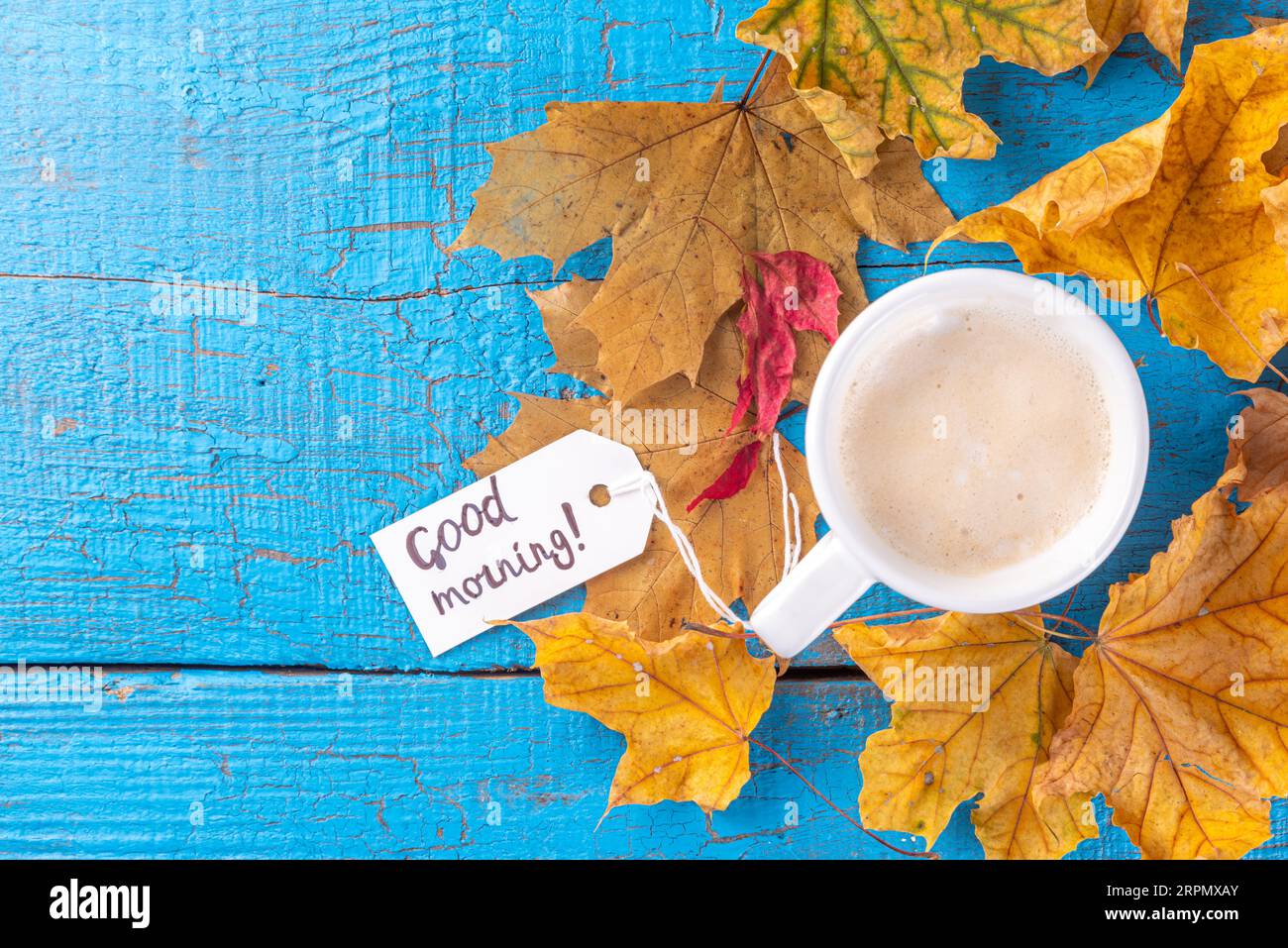 Tazza da caffè con bouquet di foglie autunnali e fiori, note di buongiorno su tavolo di legno blu turchese, dall'alto, accogliente e bella colazione autunnale Foto Stock