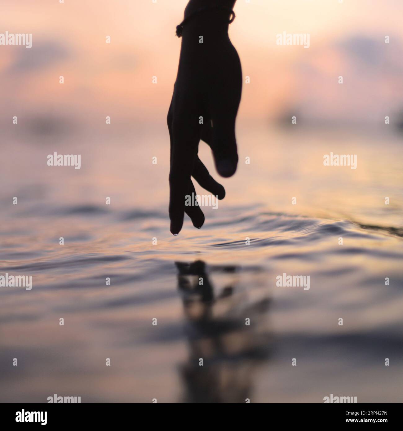 Mano femminile che tocca la calma superficie dell'acqua del lago oceanico che riflette un bellissimo tramonto estivo colorato Foto Stock