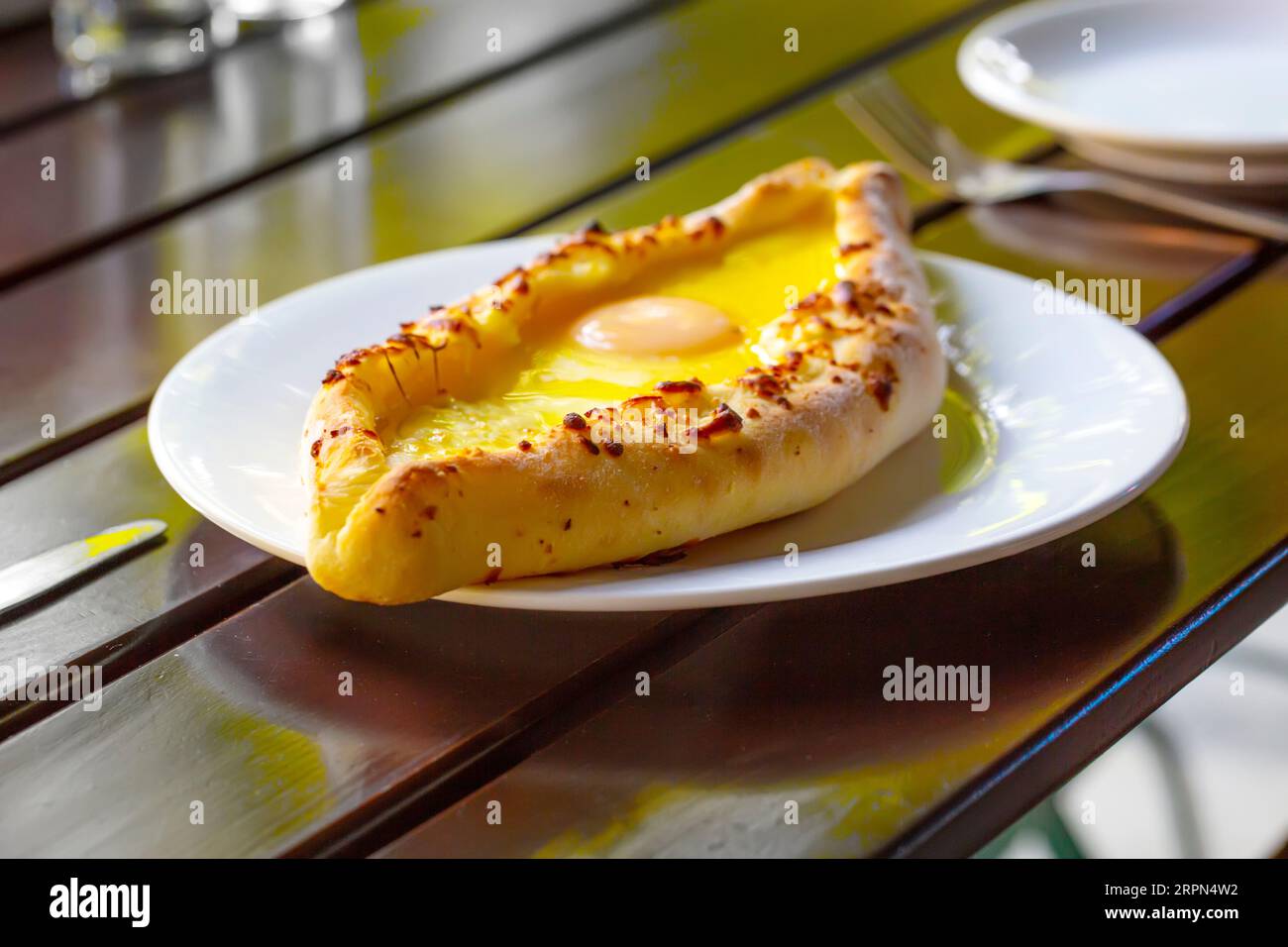 Il khachapuri in stile Adjara, impasto al forno con uovo, formaggio e due pezzi di burro su un piatto bianco in una caffetteria. Foto Stock