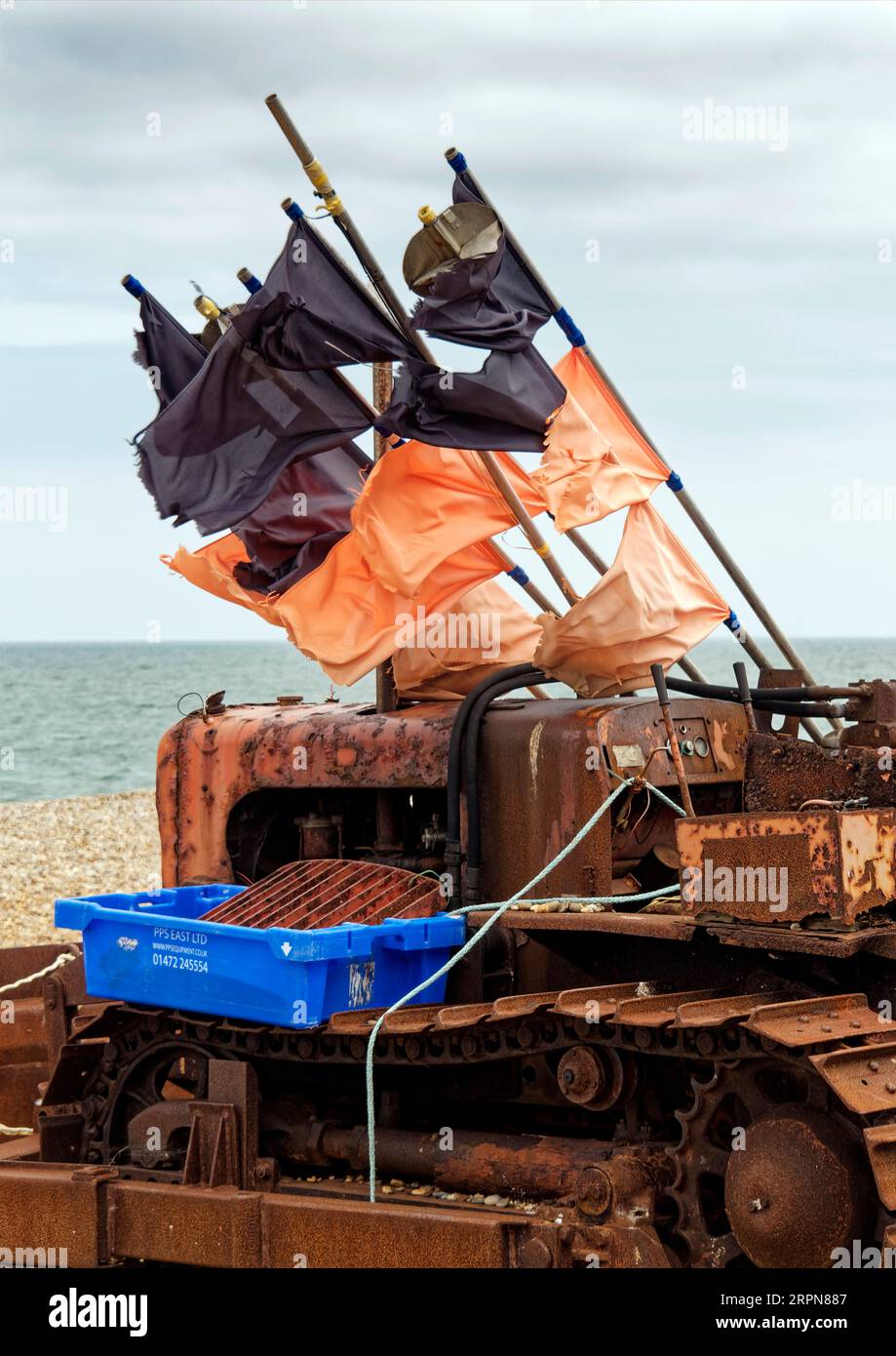 Un trattore cingolato arrugginito utilizzato per spostare i baots insieme ad attrezzi da pesca assortiti che si trovano sulla spiaggia di ciottoli di Aldeburgh nel suffolk. Foto Stock