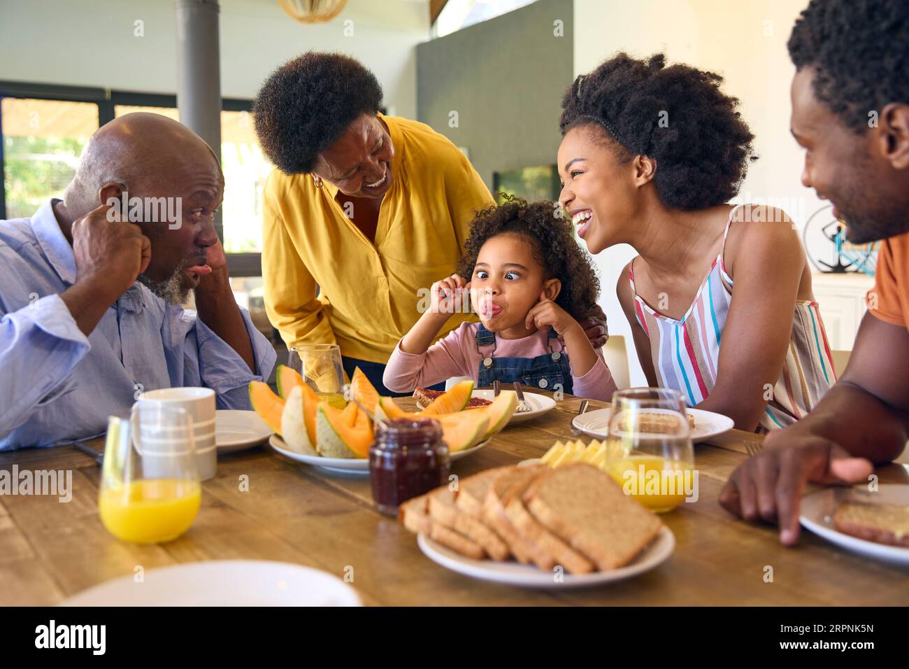 Foto di famiglia con nonni genitori e nipoti che tirano le facce a colazione intorno al tavolo a casa Foto Stock
