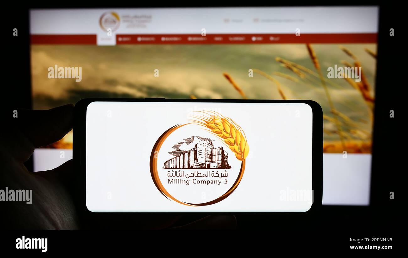 Persona che possiede il cellulare con il logo dell'azienda saudita Milling Company 3 (MC3) sullo schermo davanti alla pagina Web. Concentrarsi sul display del telefono. Foto Stock