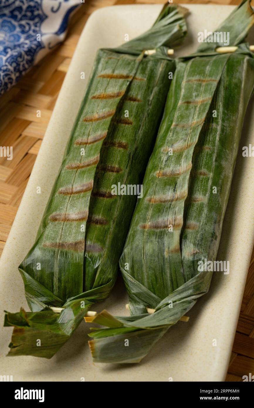 Lemper Ayam intero alla griglia avvolto in foglie di banana, uno spuntino salato indonesiano a base di riso glutinoso ripieno di pollo sminuzzato condito da vicino Foto Stock