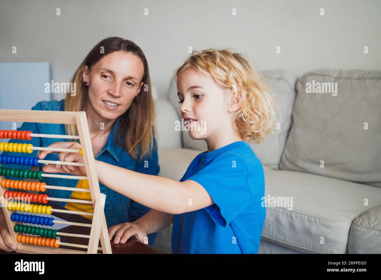 Madre e figlio che giocano insieme all'abaco all'interno del soggiorno di casa - tempo libero per la famiglia e lo studio - concetto di maternità Foto Stock