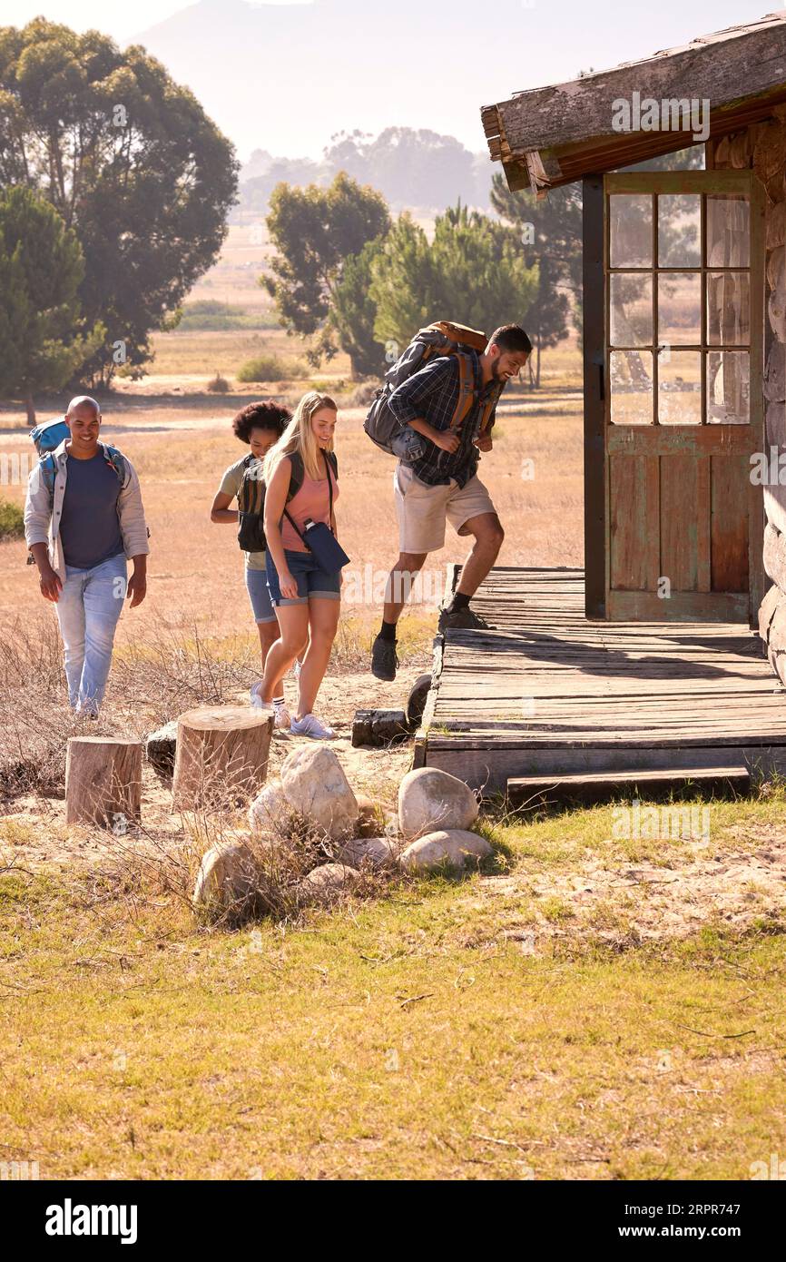 Gruppo di amici con zaini che tornano a Cabin dopo aver fatto un'escursione in campagna insieme Foto Stock