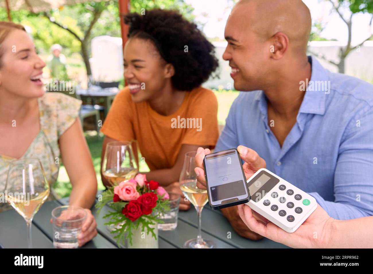 Uomo che paga il conto al bar o ristorante all'aperto utilizzando l'app Contactless sul telefono cellulare Foto Stock