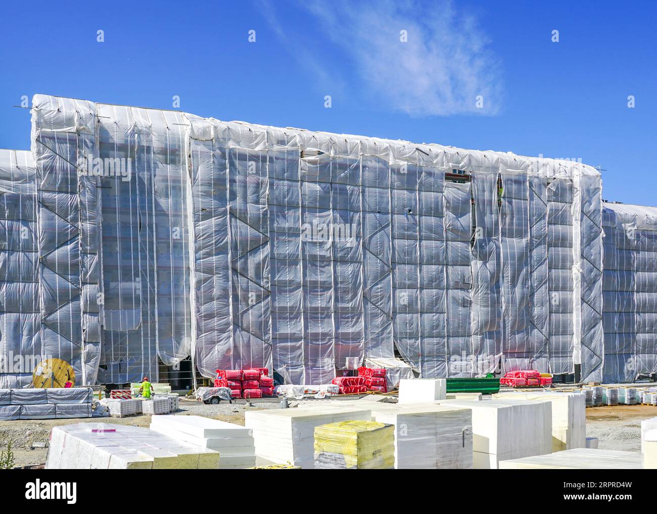 Lavori di isolamento della facciata di un edificio residenziale a più piani, facciata coperta da rete di sicurezza bianca, isolamento termico delle pareti della casa passiva esterna Foto Stock