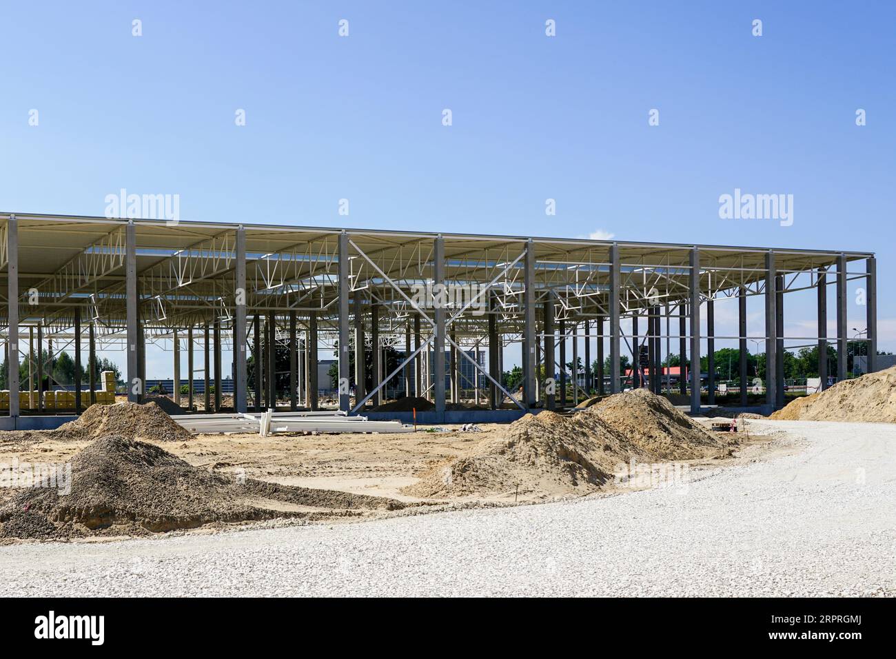 Nuova struttura in acciaio per edifici di grandi dimensioni senza finitura con tetto in acciaio ondulato su supporti in cemento armato, sfondo blu cielo Foto Stock