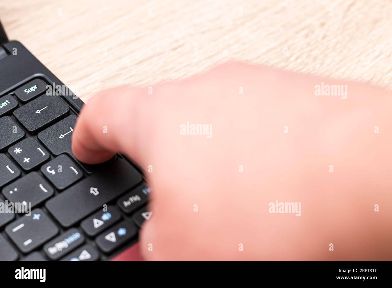 Primo piano del dito indice di una mano umana caucasica che spinge il tasto Invio sulla tastiera di un notebook sopra un tavolo di legno. Foto Stock