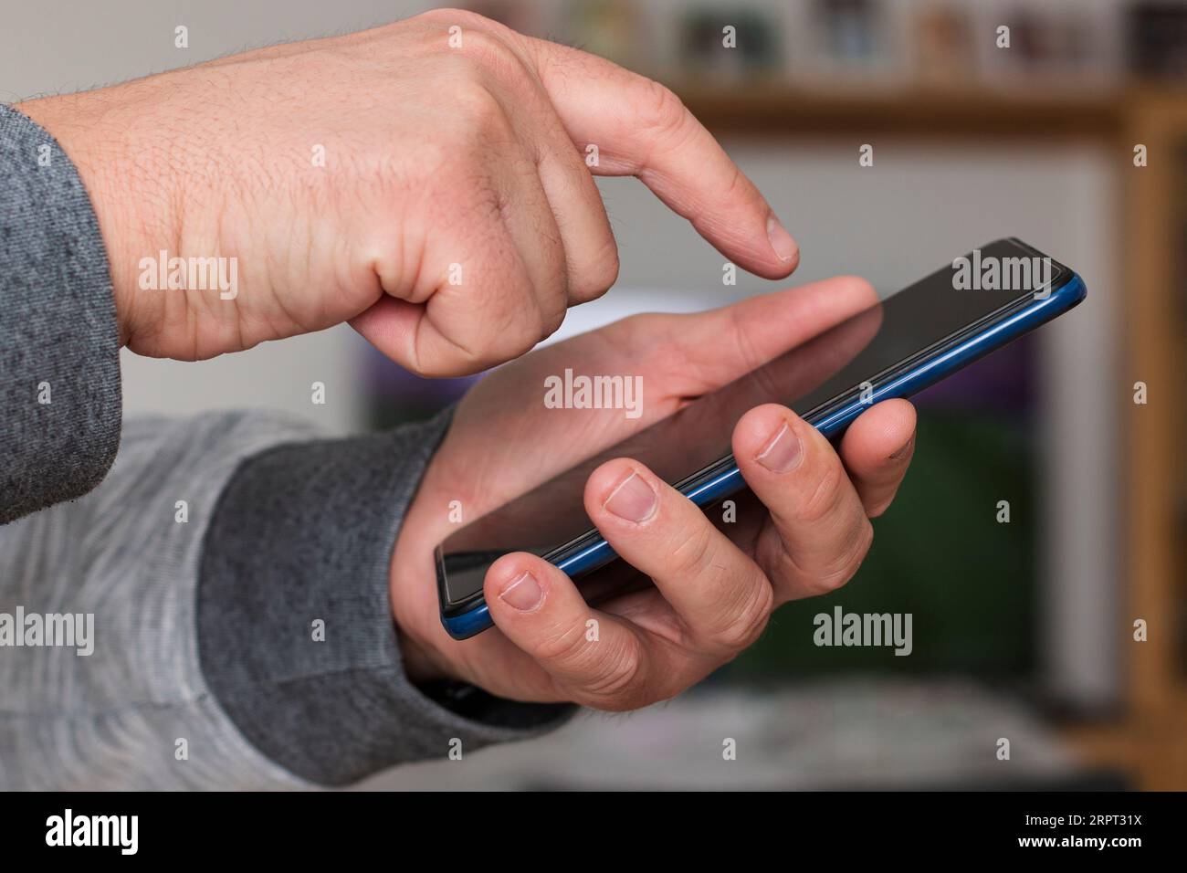 Primo piano della mano di una persona caucasica irriconoscibile che tiene e tocca lo schermo di un telefono cellulare in una casa. Foto Stock