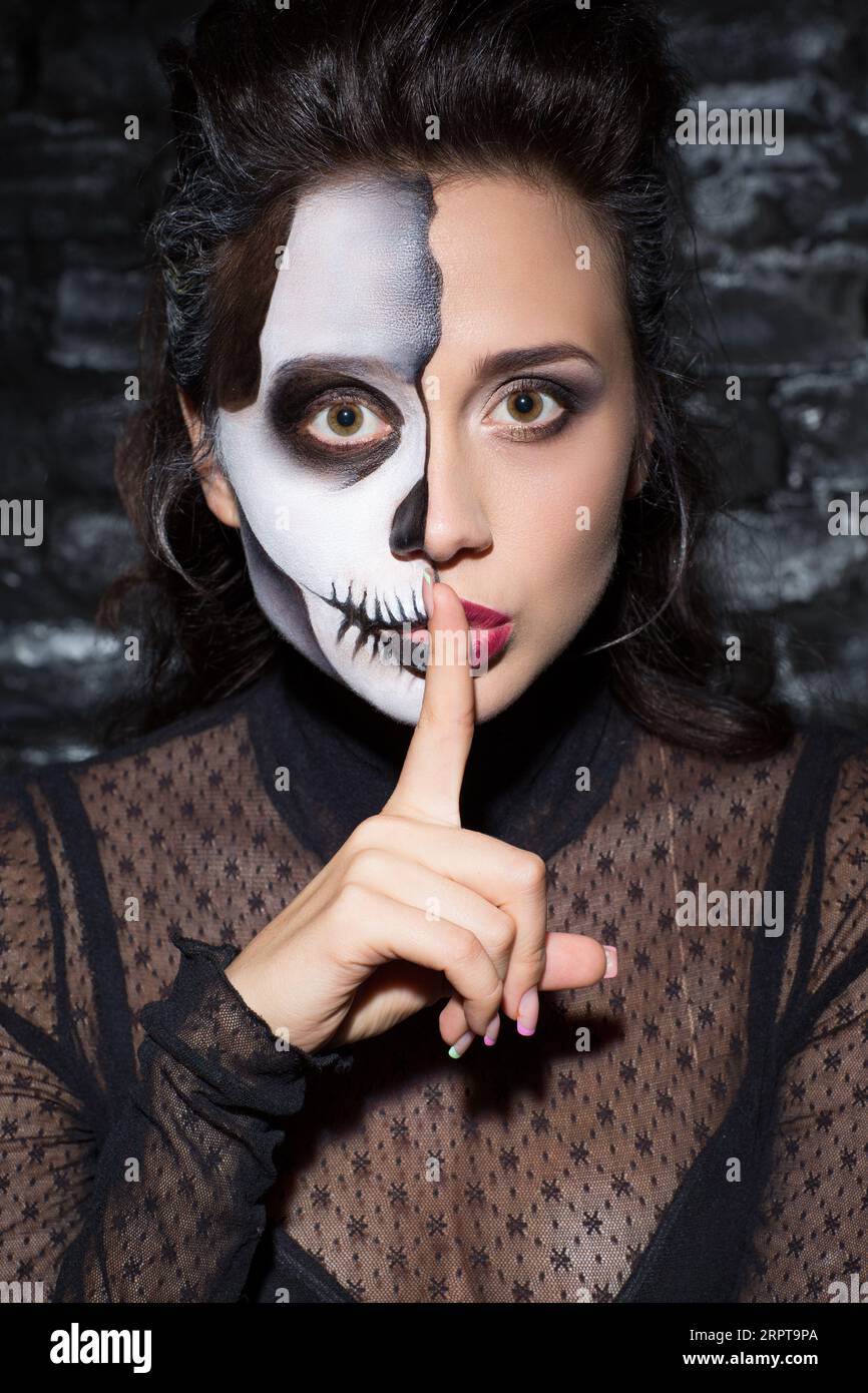 Bella femmina con mezzo trucco facciale che fa un gesto di shush. Foto Stock