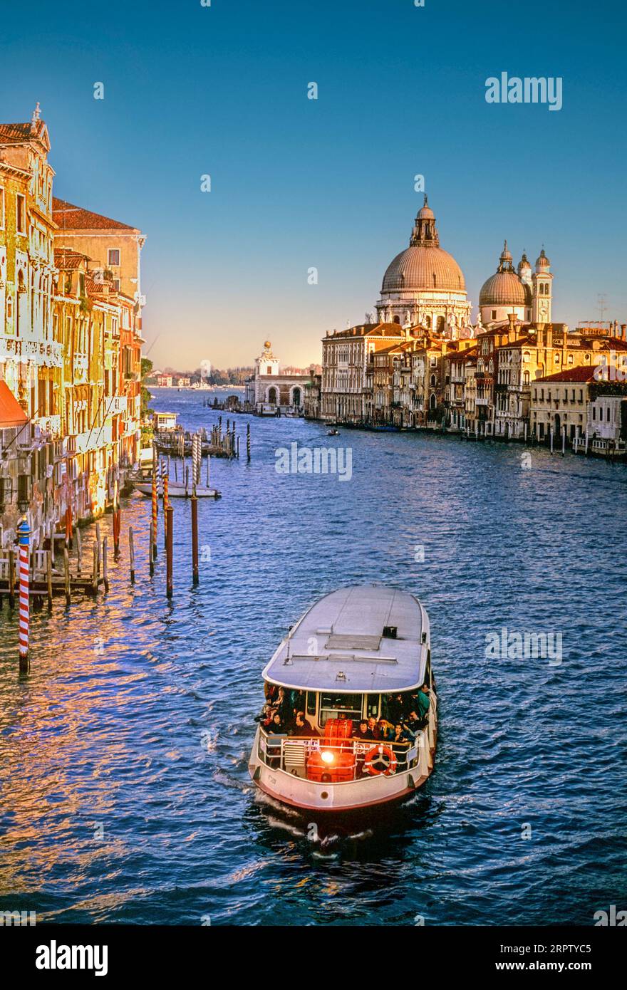 Canal grande di Venezia con vaporetto, vaporetto, vaporetto, battello, trasporto regolare in primo piano e Basilica di Santa Maria della salute alle spalle al tramonto, Venezia Italia Foto Stock