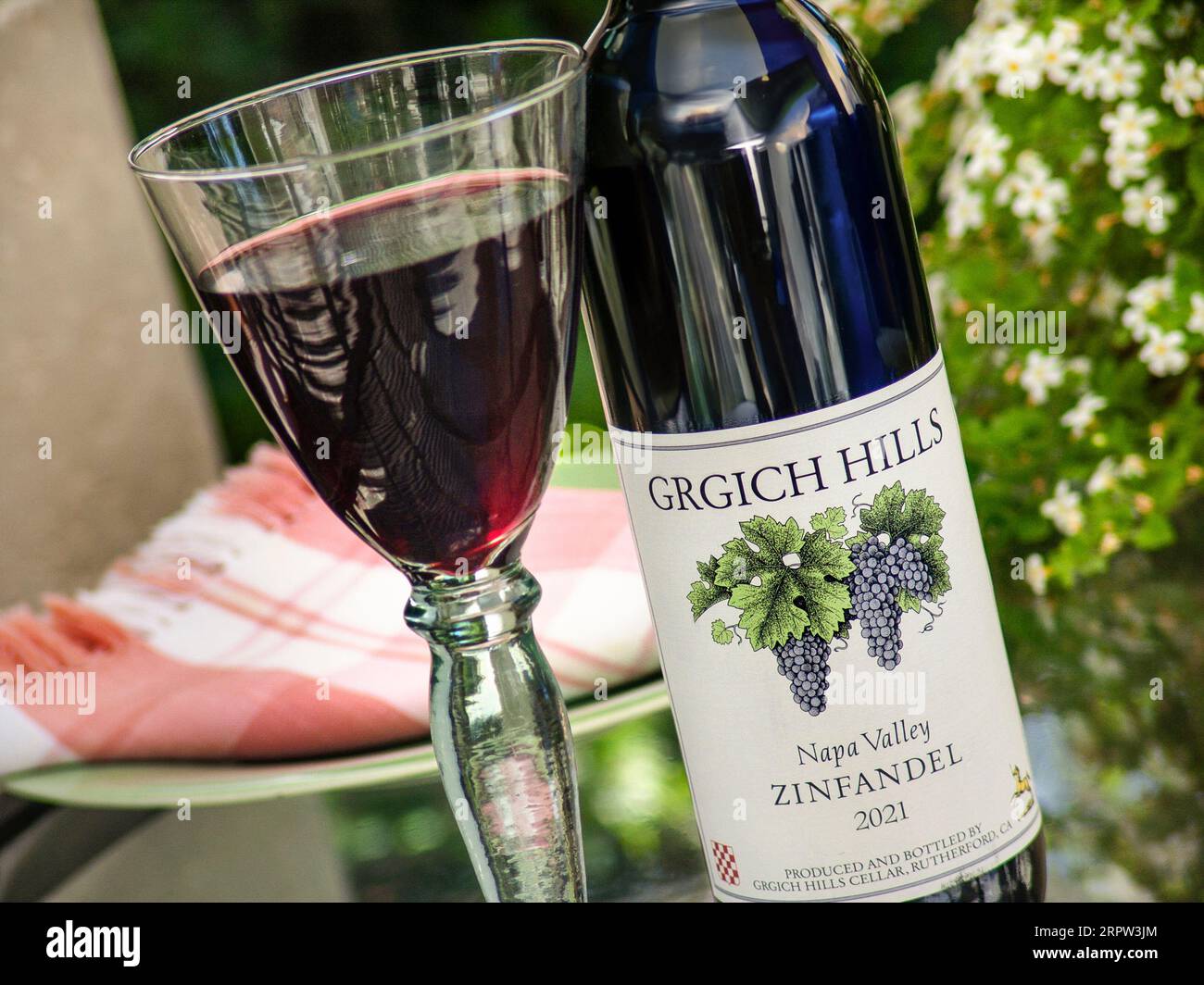 Grgich Hills Estate Zinfandel 2021 bottiglia e vetro versato sul tavolo da pranzo floreale all'aperto California USA Foto Stock