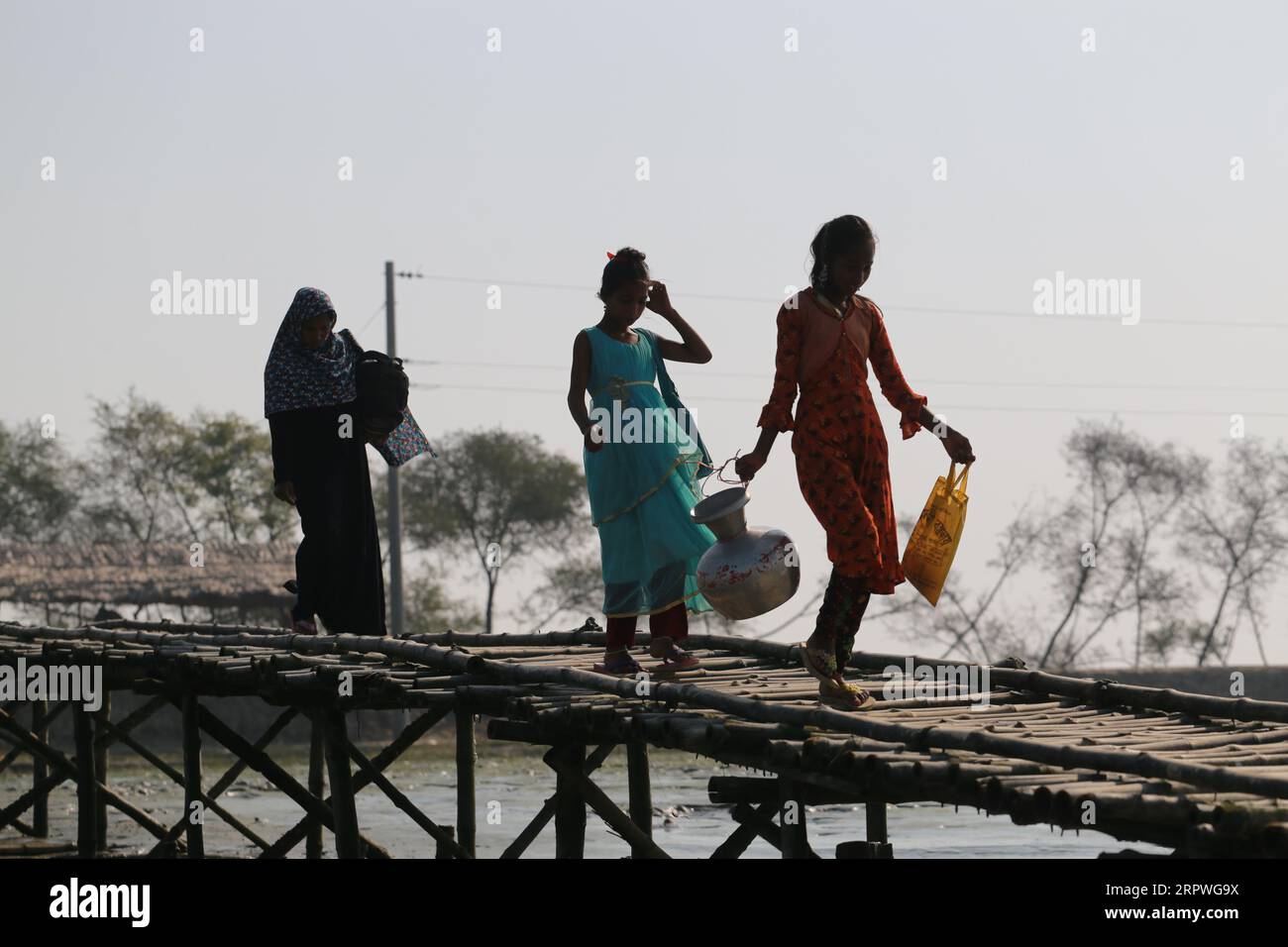 Gli abitanti del villaggio camminano su un ponte di bambù per attraversare un fiume in Bangladesh il 5 gennaio 2021. Milioni di persone sono colpite dalla crisi climatica nelle zone costiere del Bangladesh. Foto Stock