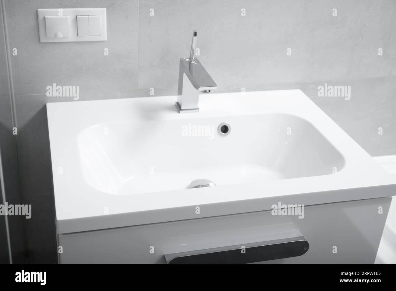 Moderno interno del bagno, lavabo bianco con cassetti, rubinetto cromato, presa e interruttore a parete. Interno del bagno con lavandino e rubinetto. Foto Stock