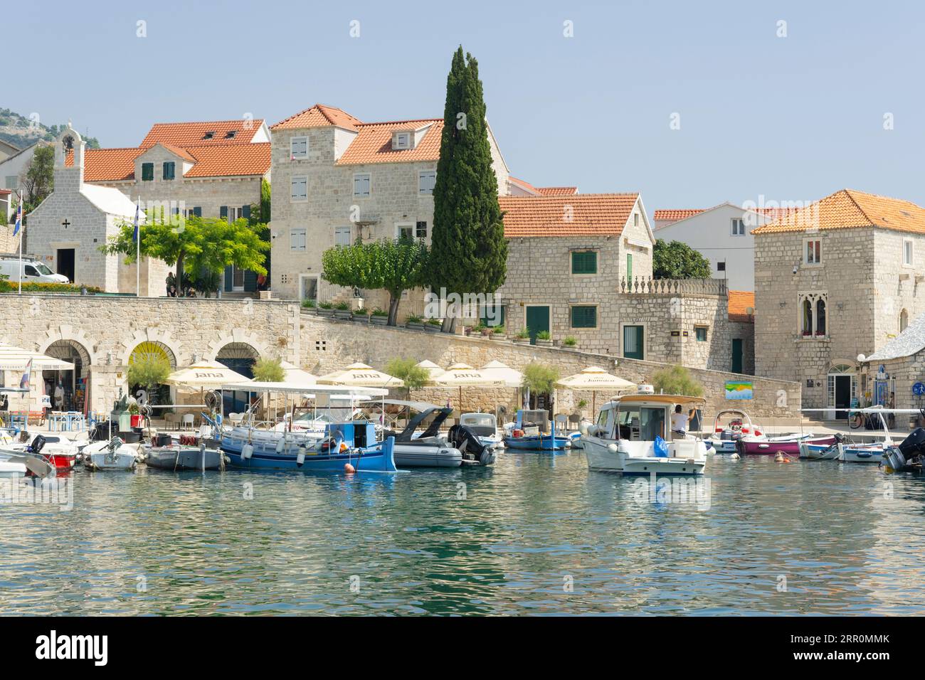 Croazia Island Brac Bol porto città portuale ormeggi sul lungomare barche a motore caffetteria ristorante ombrelloni ufficio turistico Big Blue Sports Shop Chiesa Foto Stock
