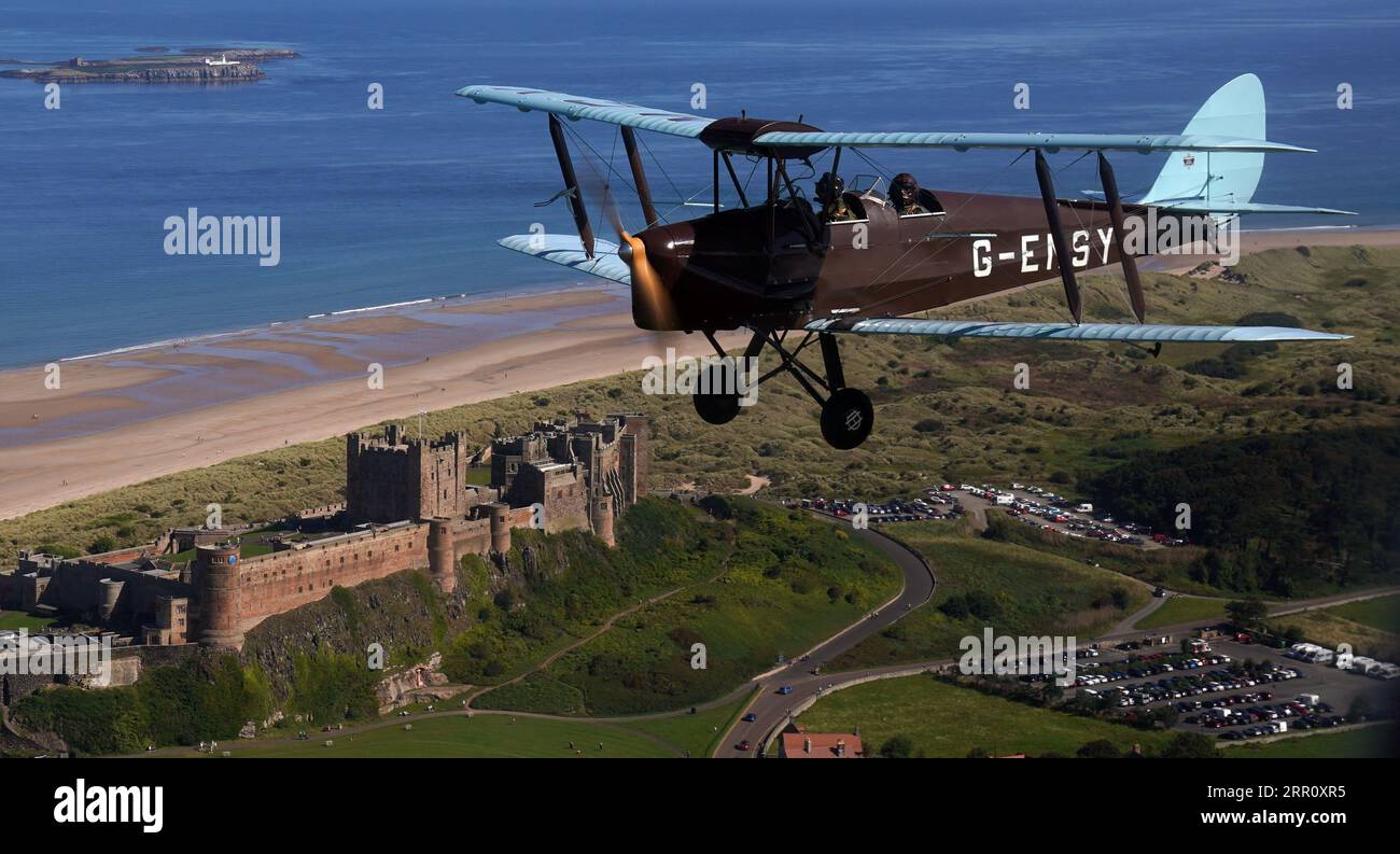 L'aereo d'epoca Tiger Moth della seconda guerra mondiale vola in cielo sopra il castello di Bamburgh nel Northumberland. Il DH82A Tiger Moth, costruito nel 1940, di proprietà di Darren Davis e Dave Burns della Tiger Flights, un'azienda indipendente con sede all'Eshott Airfield. Tempo permettendo, la G-EMSY volerà tutto l'anno, offrendo agli appassionati di aviazione l'esperienza senza precedenti di volo a cabina aperta e una vista unica del paesaggio del Northumberland e dei monumenti storici più rappresentativi. Data immagine: Martedì 5 settembre 2023. Foto Stock