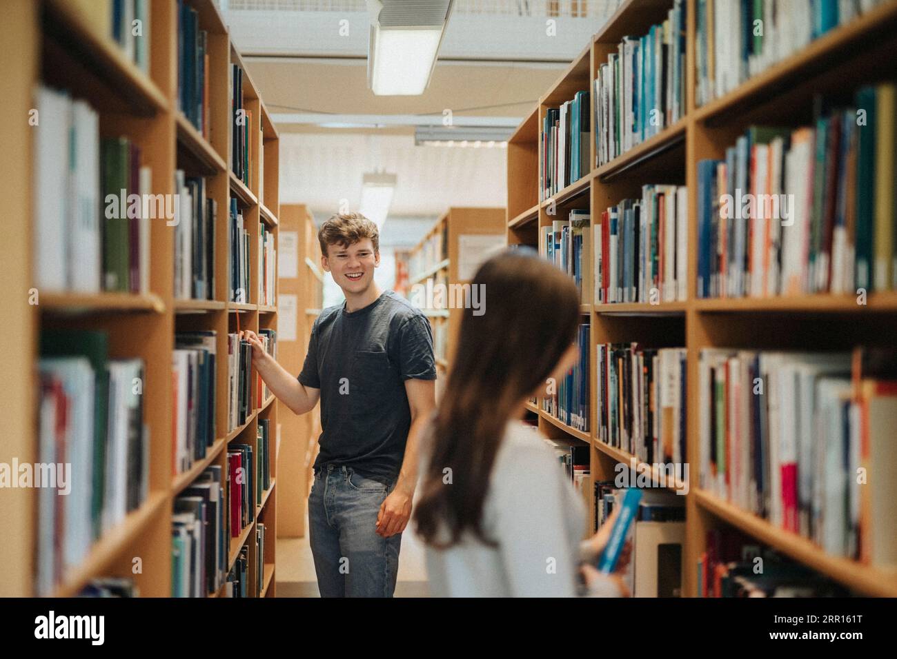 Studenti felici che cercano libri in libreria in biblioteca all'università Foto Stock