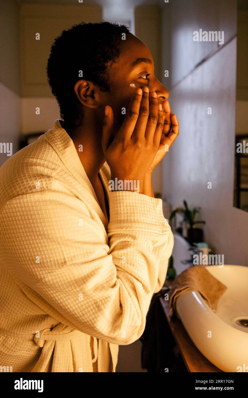 Giovane donna che applica idratante sul viso a casa Foto Stock