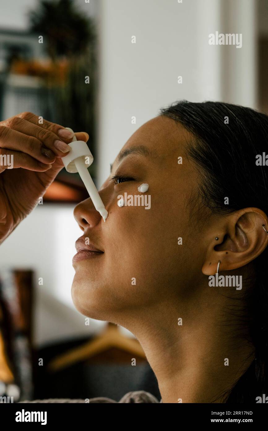 Giovane donna sorridente che applica crema sul viso Foto Stock