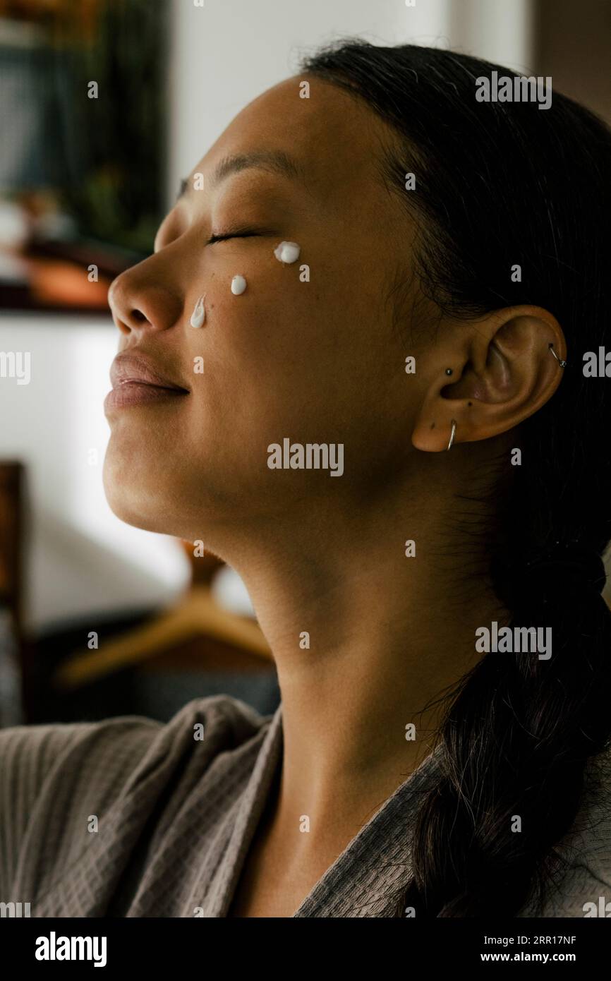 Giovane donna con gli occhi chiusi e crema sul viso Foto Stock