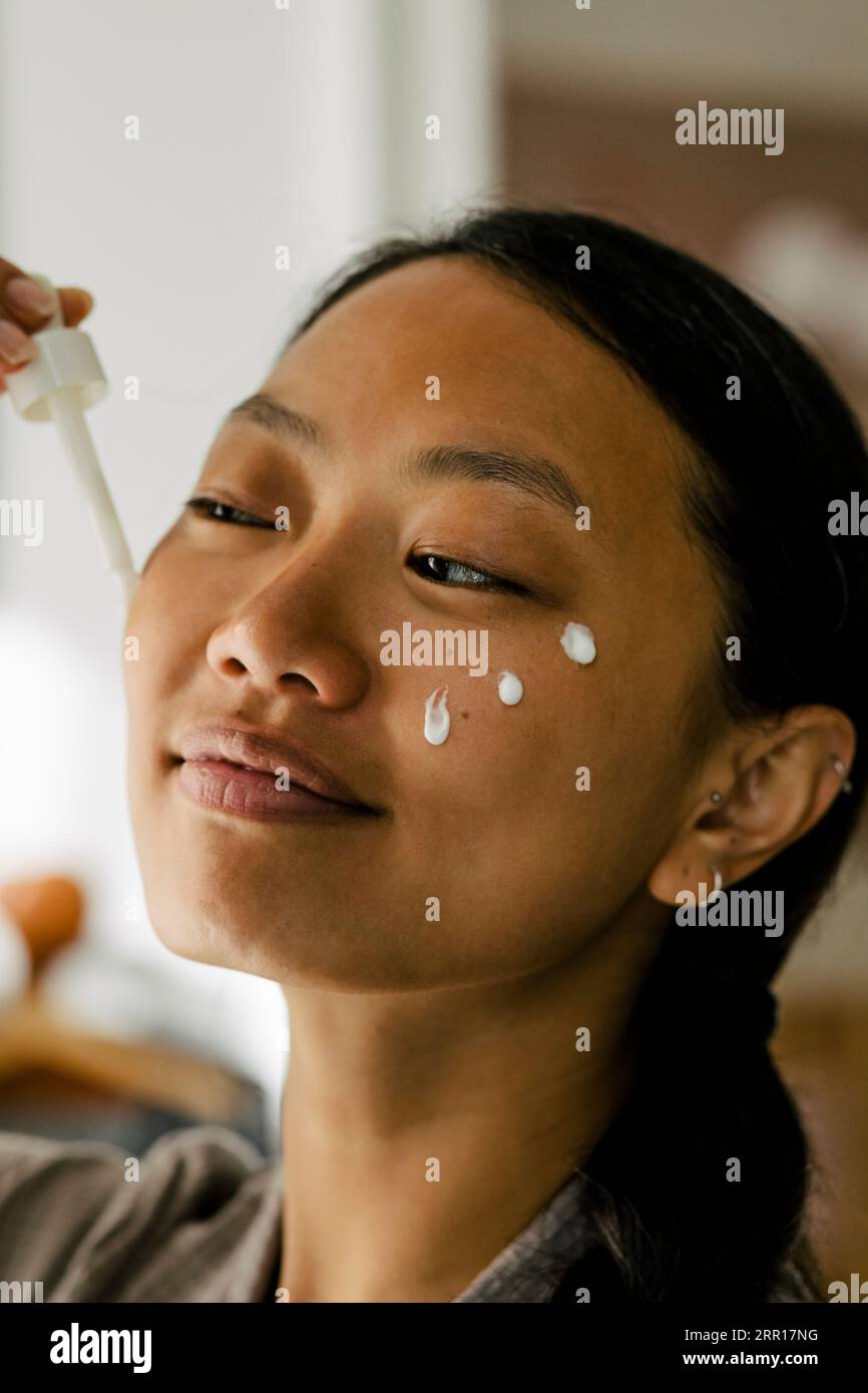 Donna sorridente che applica la crema sul viso Foto Stock