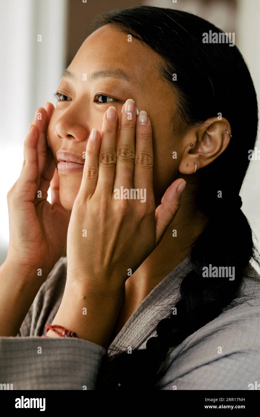 Giovane donna che applica idratante sul viso a casa Foto Stock