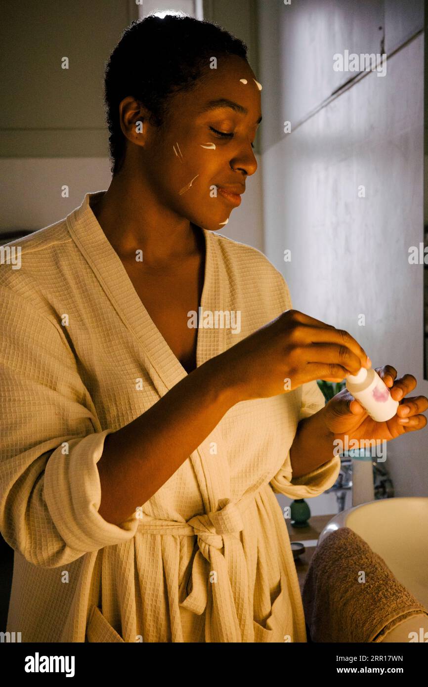 Giovane donna che applica prodotti di bellezza sul viso Foto Stock