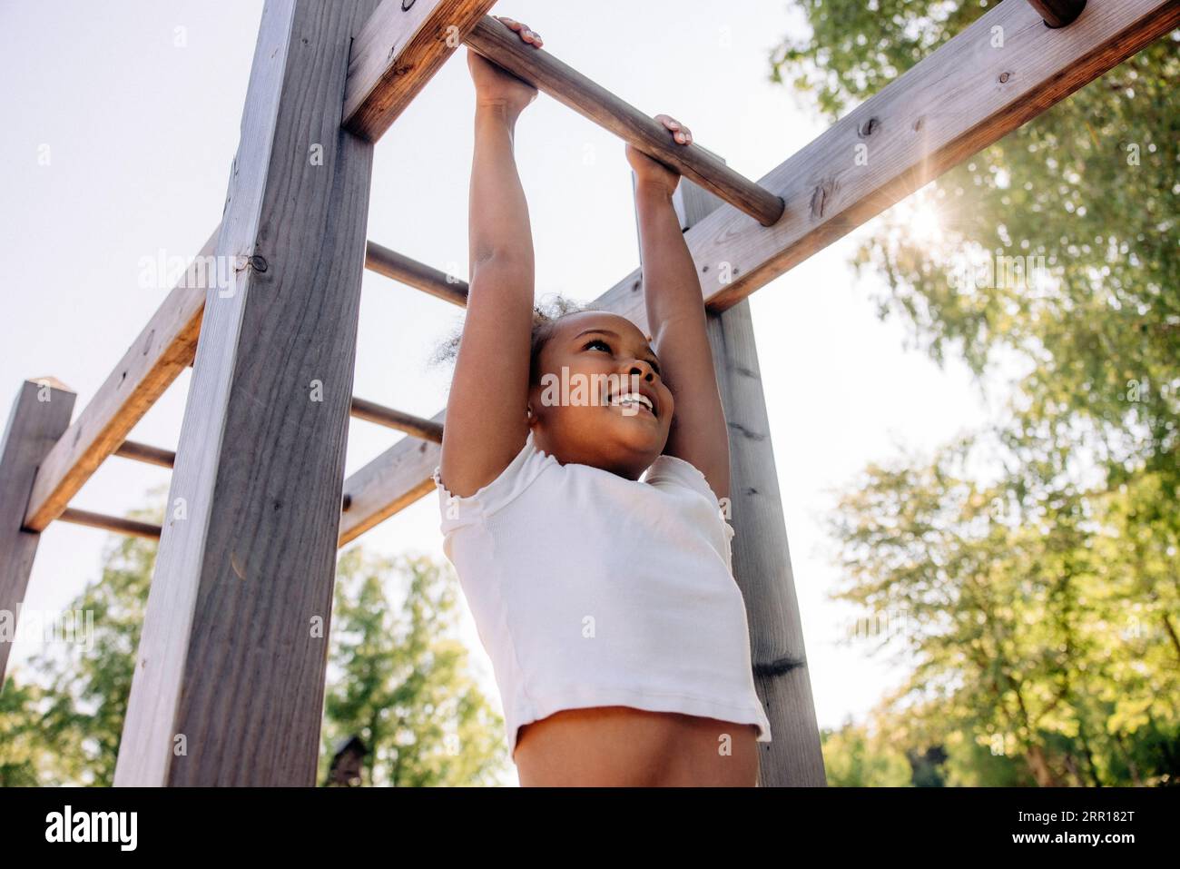 Vista dall'angolo basso di una ragazza sorridente che si appende mentre fa scimmie al campo estivo Foto Stock