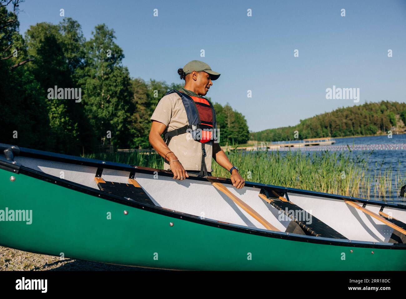 Consigliere maschile che indossa un giubbotto salvagente che tiene un kayak vicino al lago al campo estivo Foto Stock