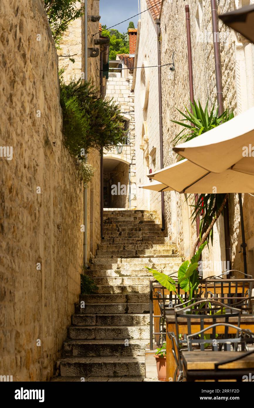 Croazia Isola di Hvar città vecchia vicolo stretto gradini ripidi verso Cittadella tavoli sedie bar caffetteria ombrelloni muri di pietra piante pittoresche Foto Stock