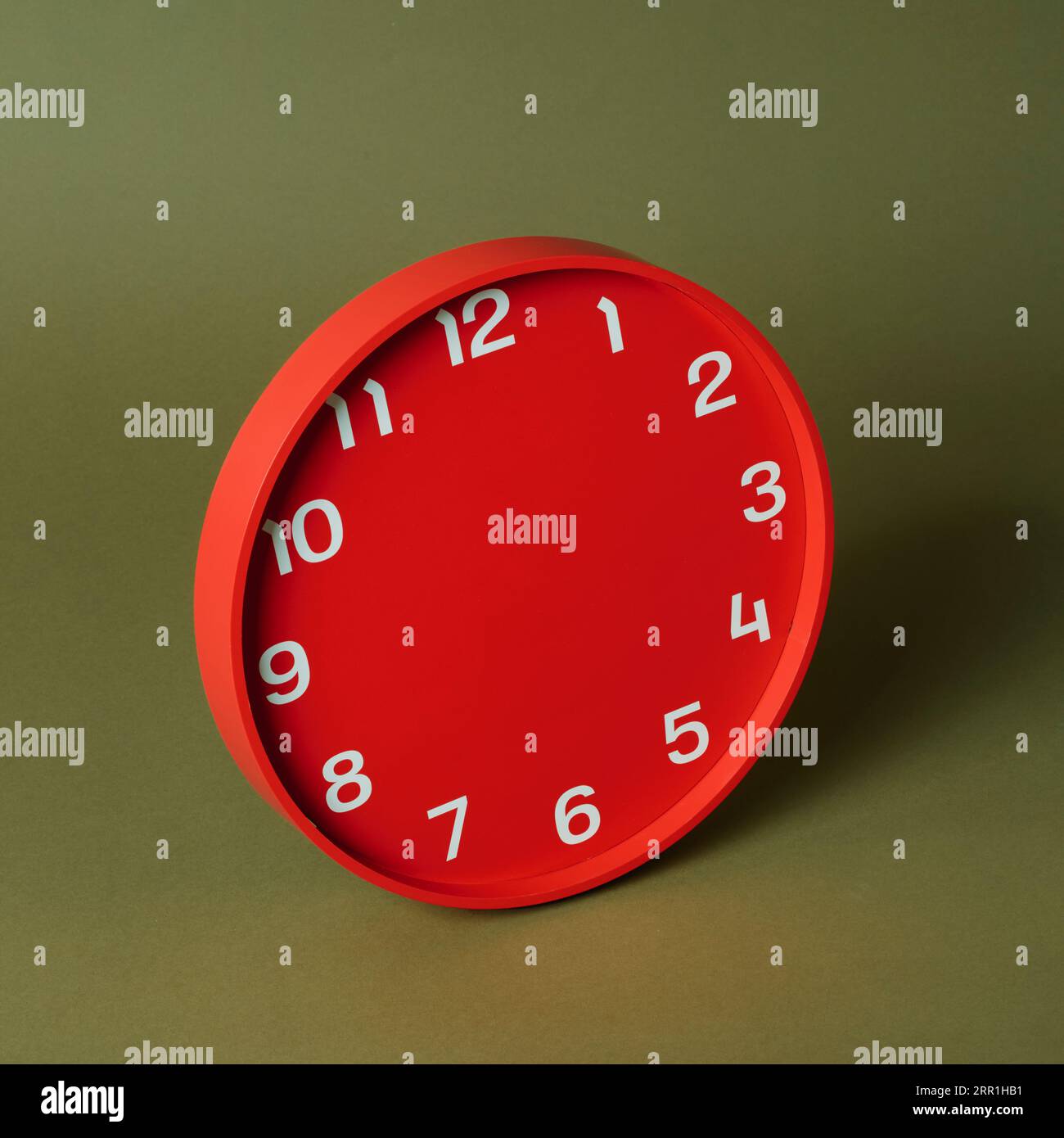 primo piano di un orologio rosso senza lancette di ore o minuti su uno sfondo verde oliva Foto Stock