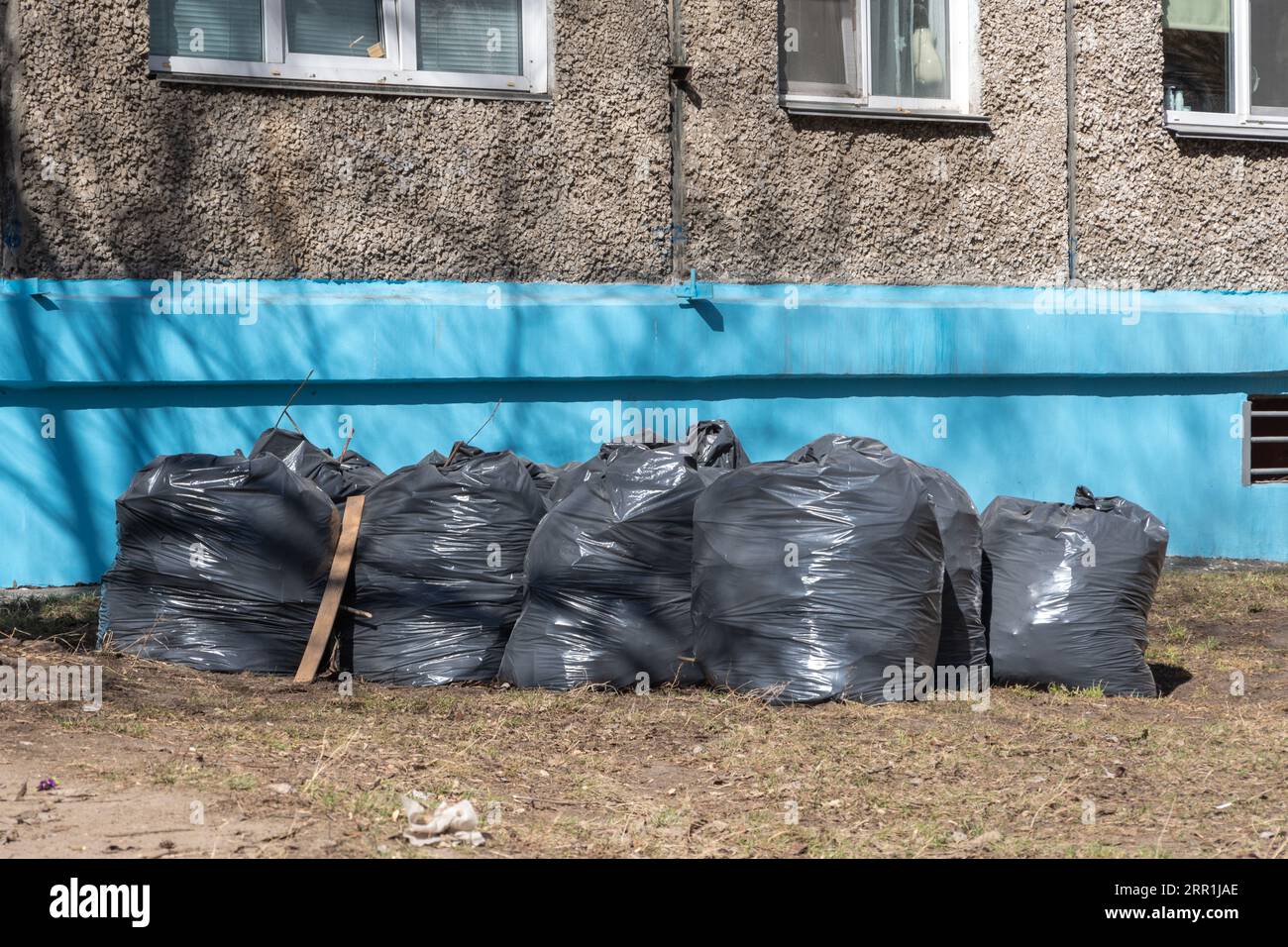 Sacchetti di plastica neri pieni di spazzatura primaverile in piedi lungo la parete blu della casa. Pulizia di primavera. Il concetto di raccolta rifiuti, ecologia, envi Foto Stock