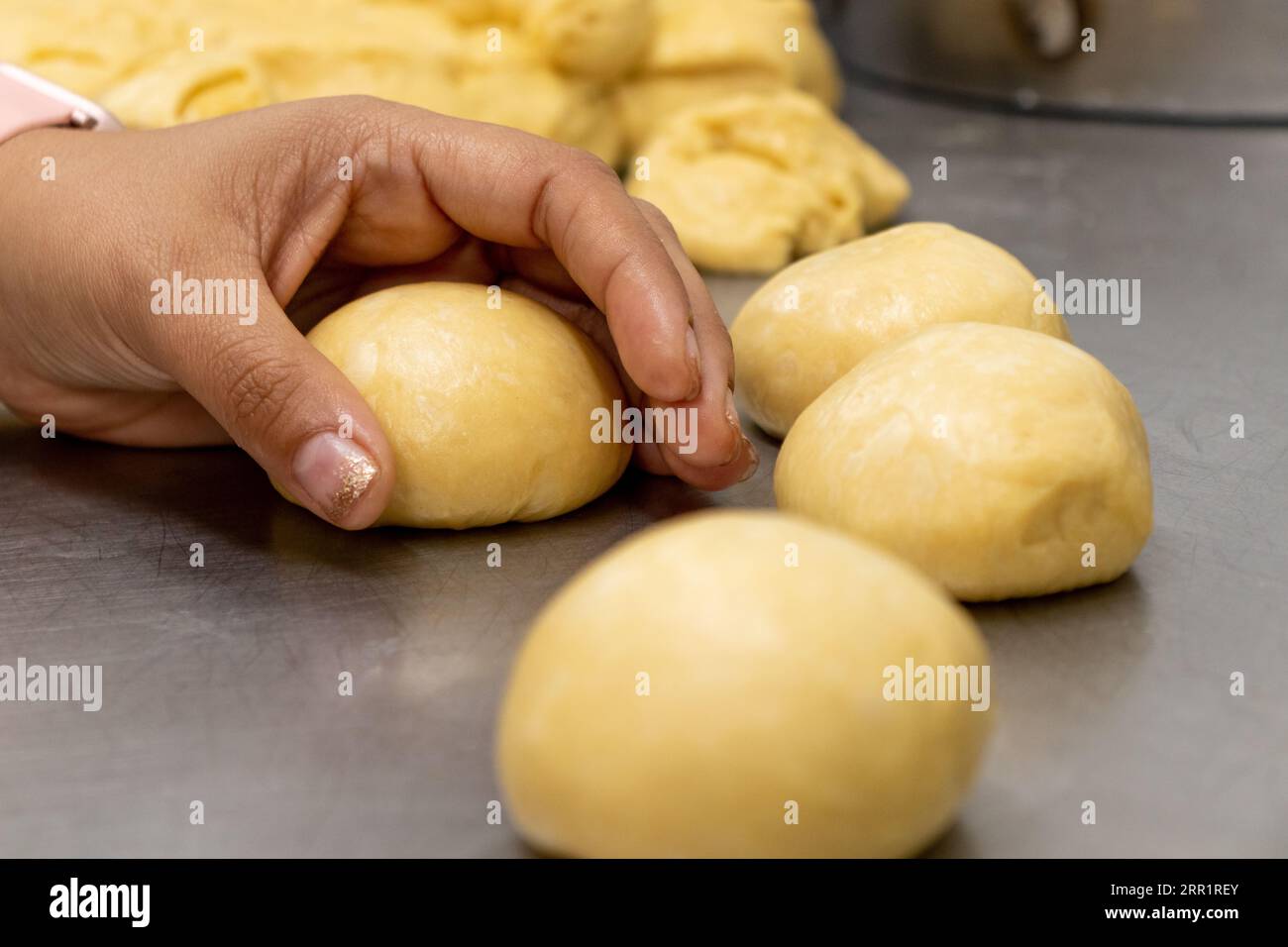 Coltivate un panettiere nero anonimo, preparando un impasto di pane rotondo crudo da grumi di farina mista su un tavolo metallico in una moderna panetteria Foto Stock
